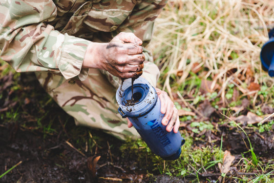 Person in camouflage gear using a water filter in a natural setting