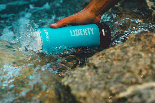 Blue Liberty bottle being submerged in water with a hand holding it.