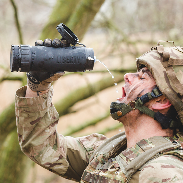 Person in military gear drinking from a Liberty water bottle outdoors.